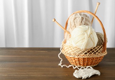 Skeins of soft yarn, knitting sample and needles in basket on wooden table indoors, space for text