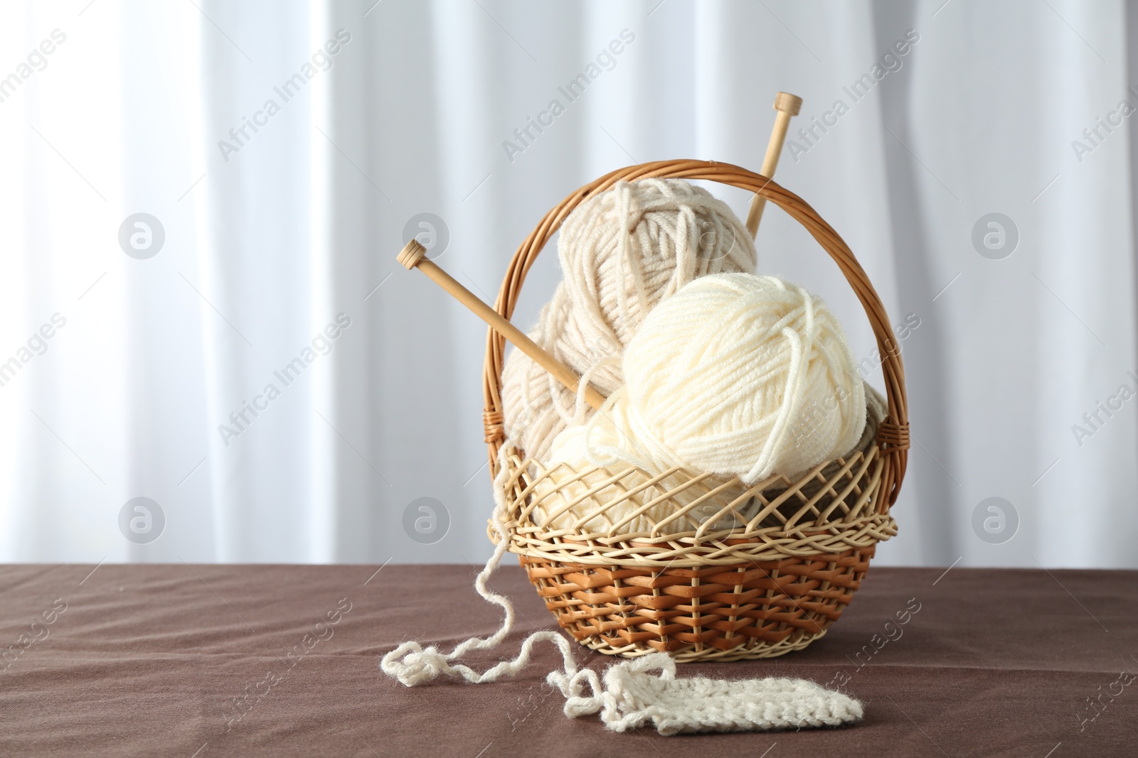 Photo of Skeins of soft yarn, knitting sample and needles in basket on brown fabric indoors