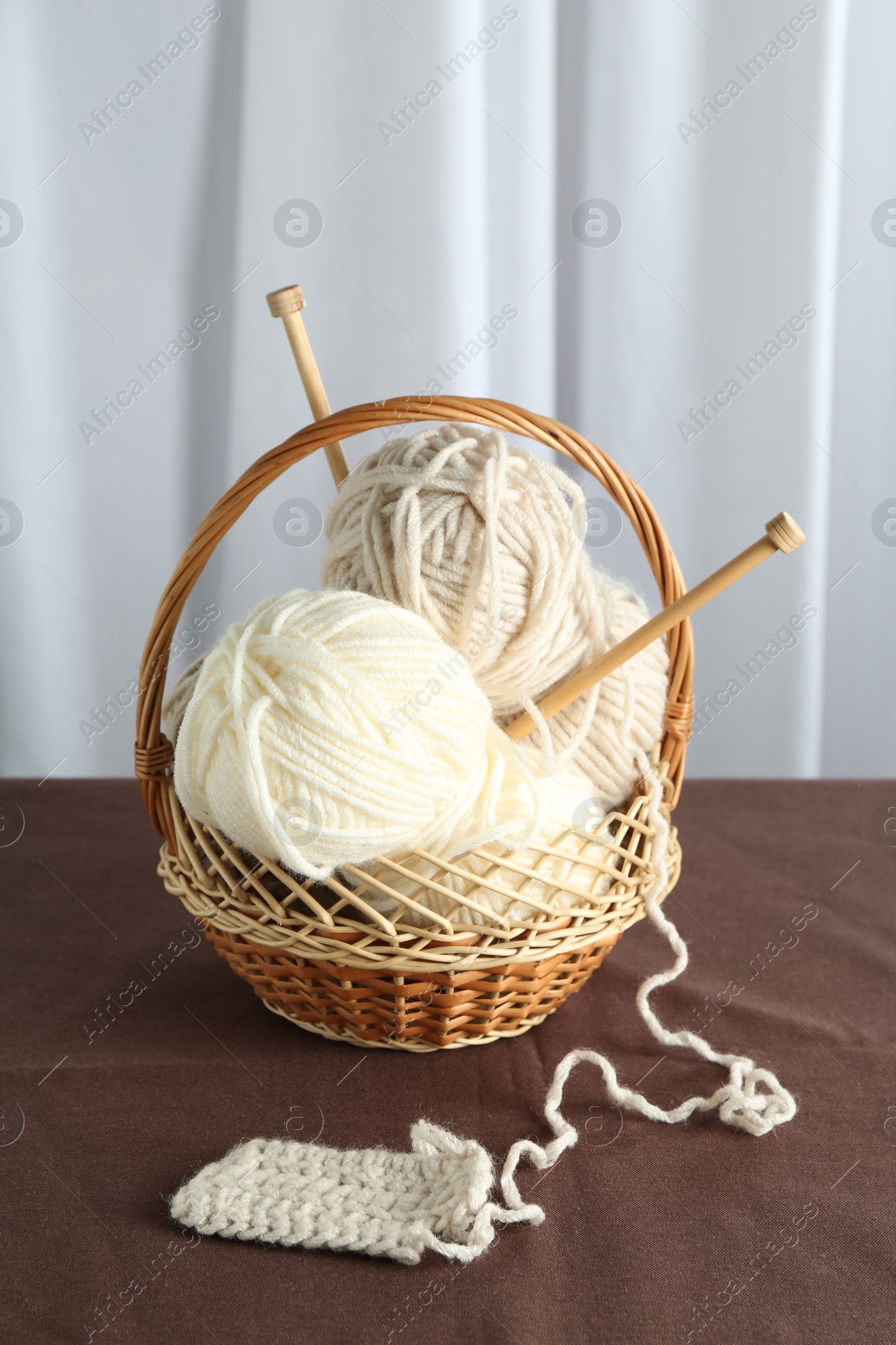 Photo of Skeins of soft yarn, knitting sample and needles in basket on brown fabric indoors