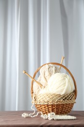 Photo of Skeins of soft yarn, knitting sample and needles in basket on brown fabric indoors