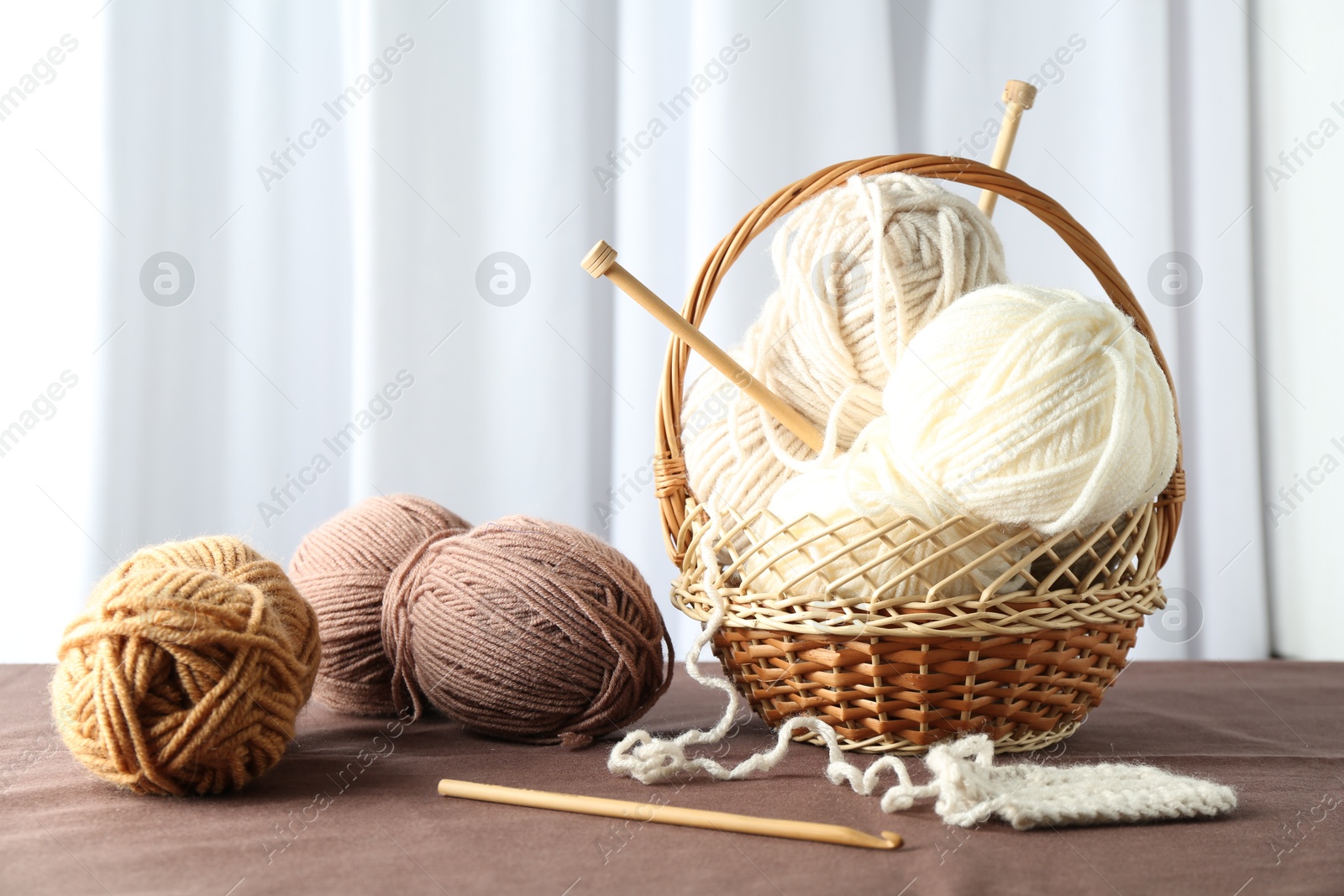 Photo of Skeins of soft yarn, knitting sample and needles on brown fabric indoors