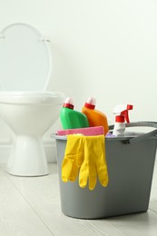 Bucket with different toilet cleaners, rag and gloves on floor in bathroom