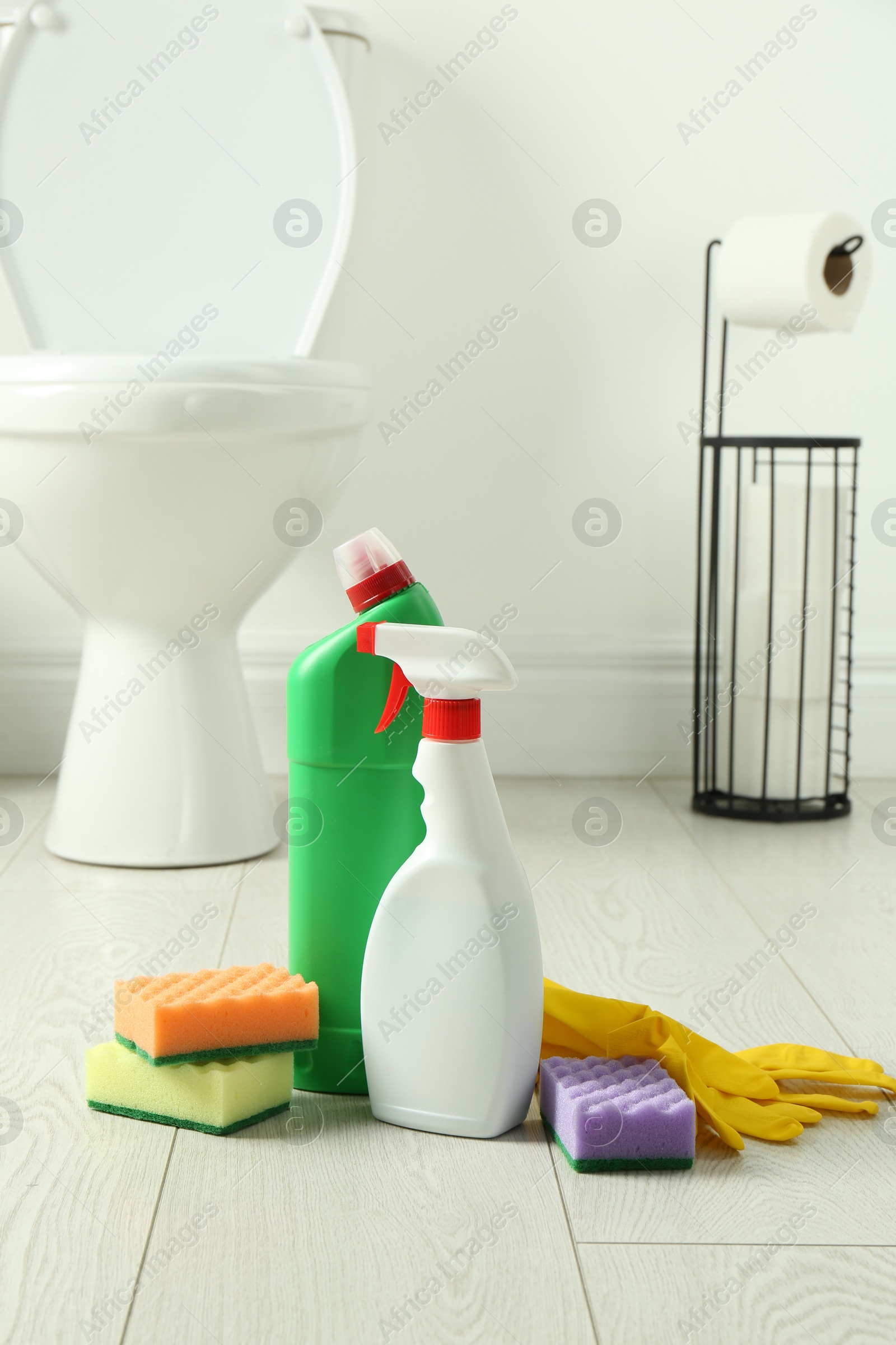 Photo of Toilet cleaners, sponges and gloves on floor in bathroom