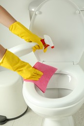 Woman with spray and rag cleaning toilet seat in bathroom, closeup