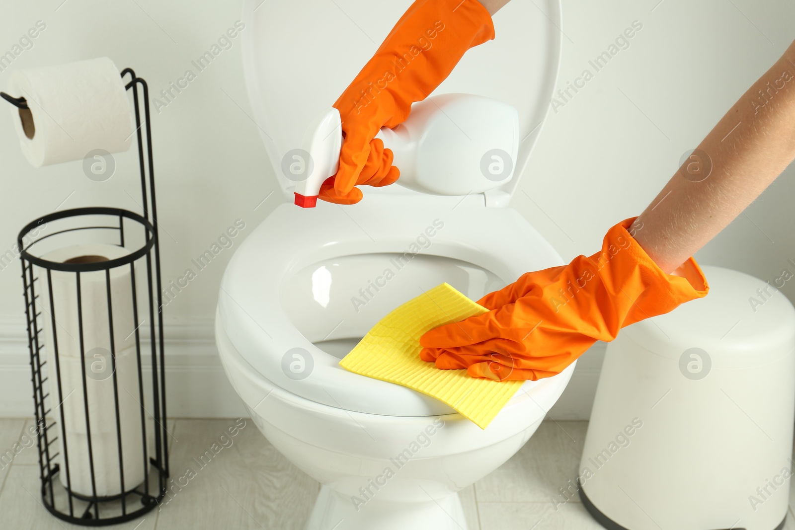 Photo of Woman with spray and rag cleaning toilet seat in bathroom, closeup