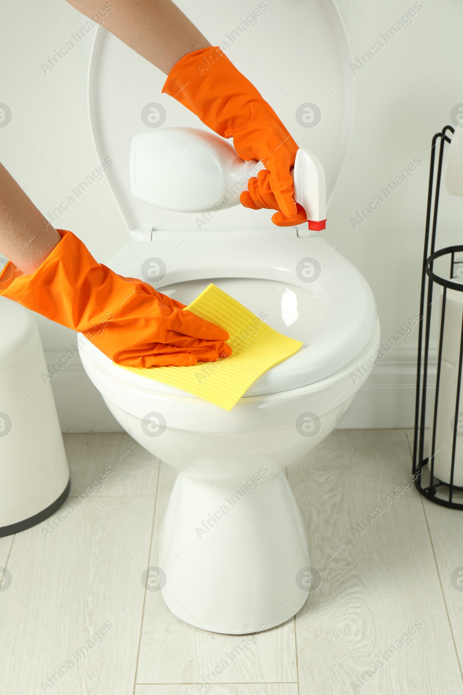 Photo of Woman with spray and rag cleaning toilet seat in bathroom, closeup