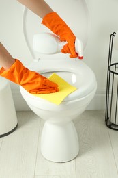 Woman with spray and rag cleaning toilet seat in bathroom, closeup