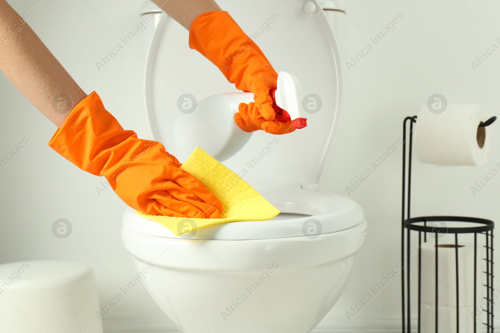 Photo of Woman with spray and rag cleaning toilet seat in bathroom, closeup