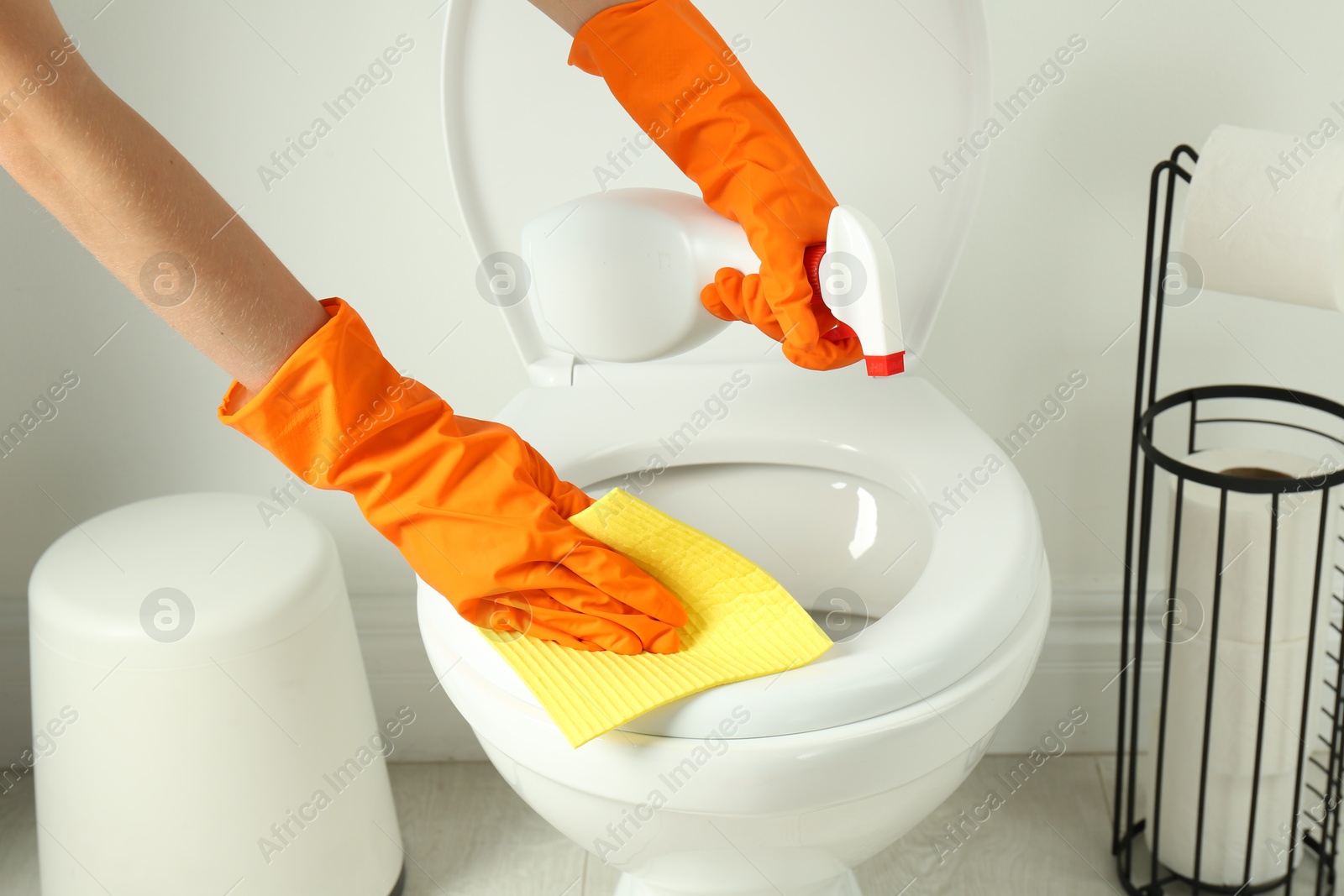 Photo of Woman with spray and rag cleaning toilet seat in bathroom, closeup