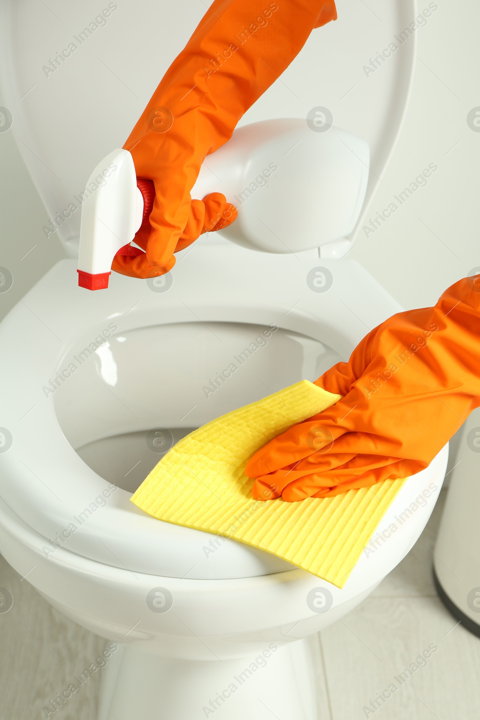 Photo of Woman with spray and rag cleaning toilet seat in bathroom, closeup