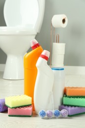 Photo of Toilet cleaners, sponges and trash bags on floor in bathroom, closeup