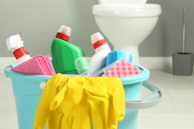 Photo of Bucket with different toilet cleaners, rag, sponge and gloves in bathroom, closeup