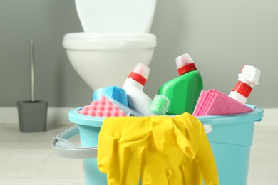 Photo of Bucket with different toilet cleaners, rag, sponge and gloves in bathroom, closeup