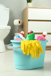 Photo of Bucket with different toilet cleaners, rag, sponge and gloves on floor in bathroom