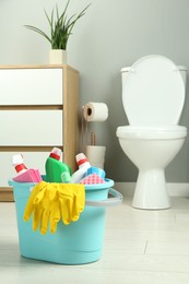 Photo of Bucket with different toilet cleaners, rag, sponge and gloves on floor in bathroom