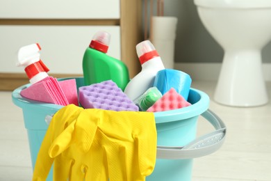 Photo of Bucket with different toilet cleaners, rag, sponge and gloves in bathroom, closeup