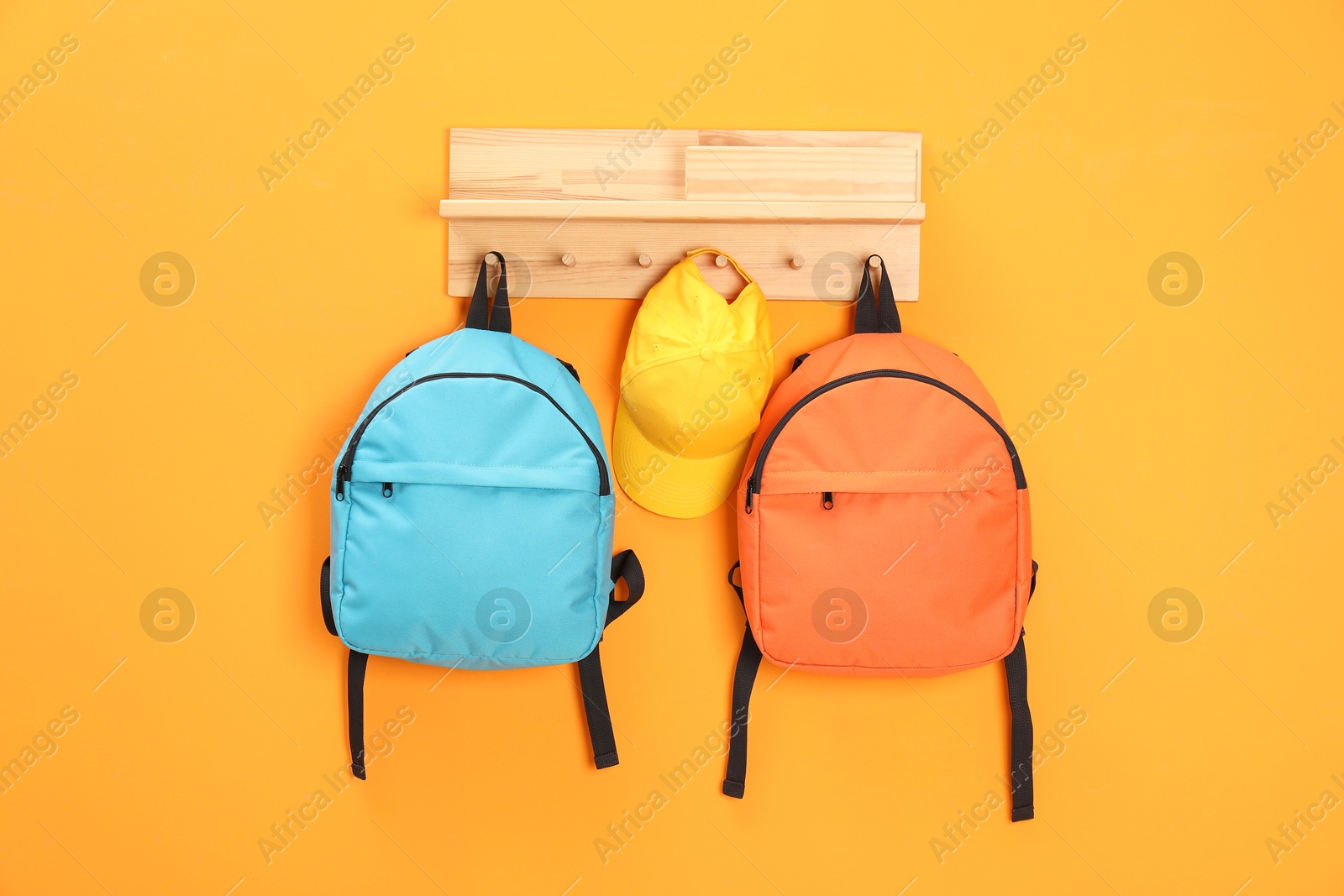 Photo of Bright backpacks and cap hanging on orange wall