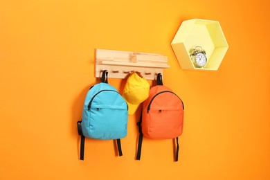 Photo of Bright backpacks, cap and alarm clock on orange wall