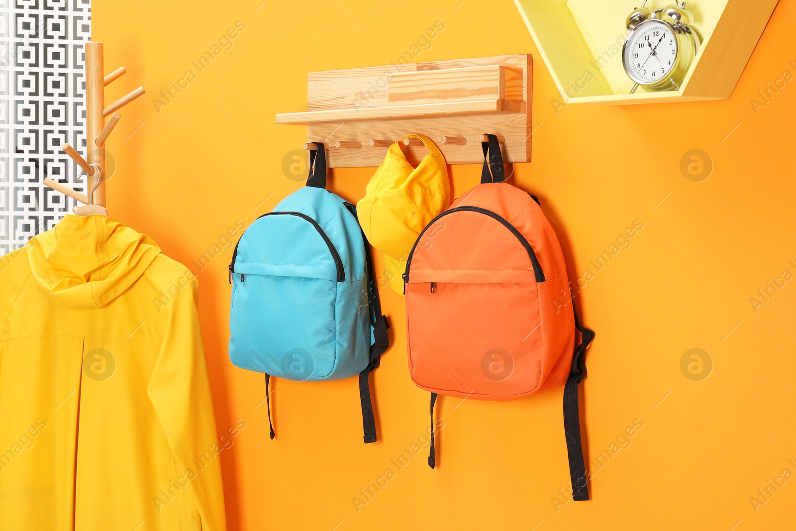 Photo of Bright backpacks, cap, coat and alarm clock near orange wall