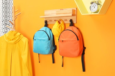 Photo of Bright backpacks, cap, coat and alarm clock near orange wall