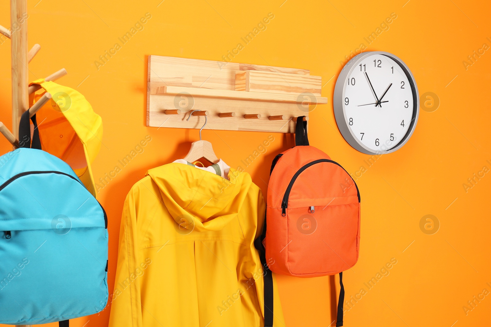 Photo of Bright backpacks, cap, coat and clock near orange wall