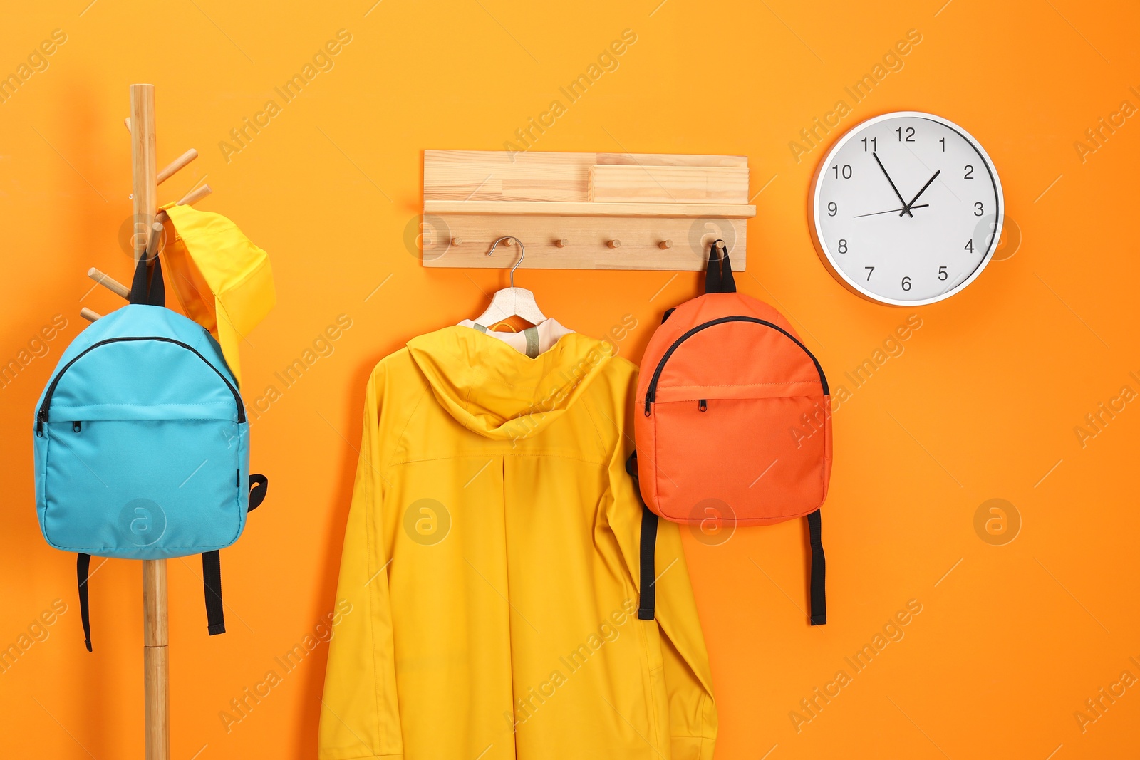 Photo of Bright backpacks, cap, coat and clock near orange wall