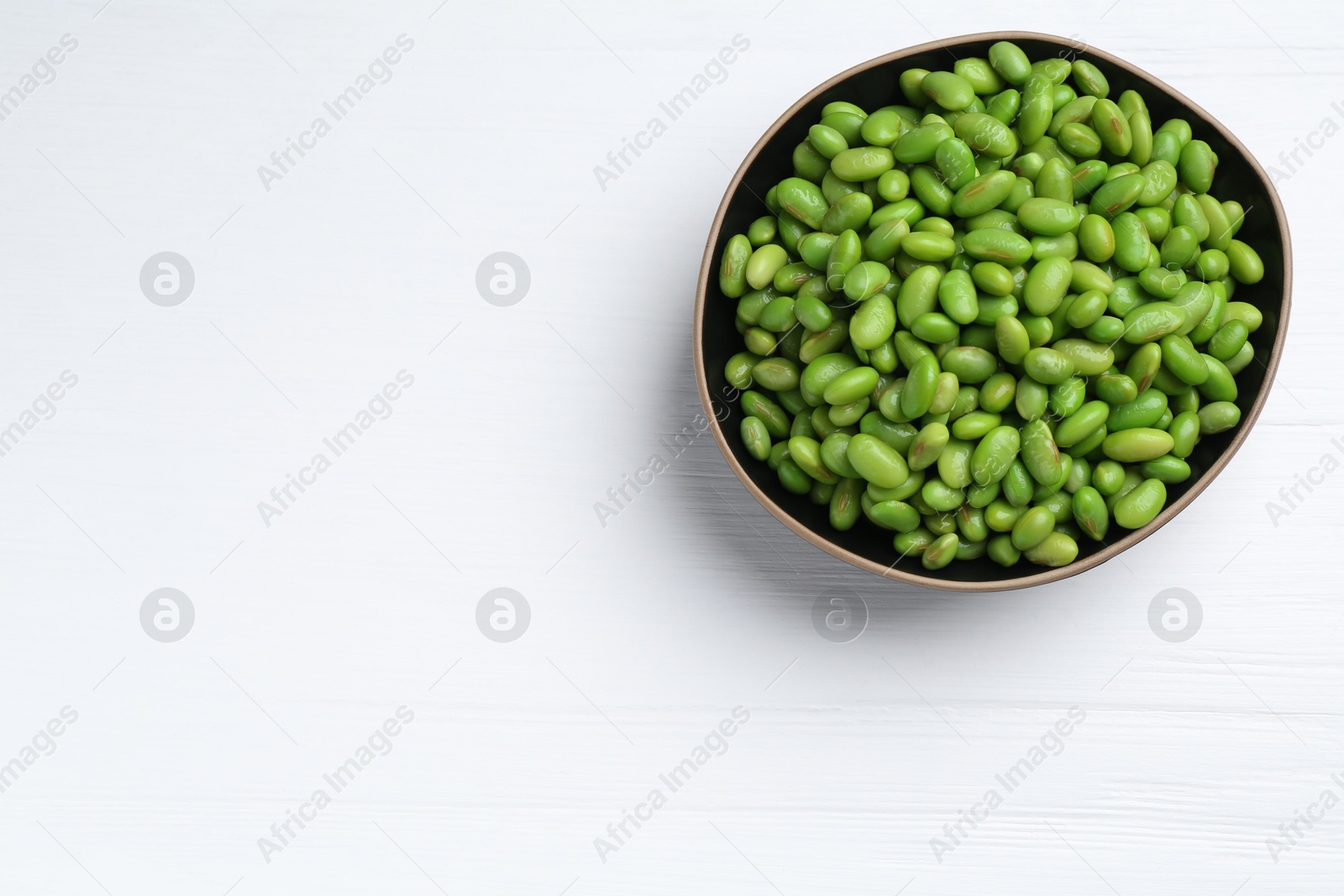 Photo of Fresh edamame soybeans in bowl on white wooden table, top view. Space for text