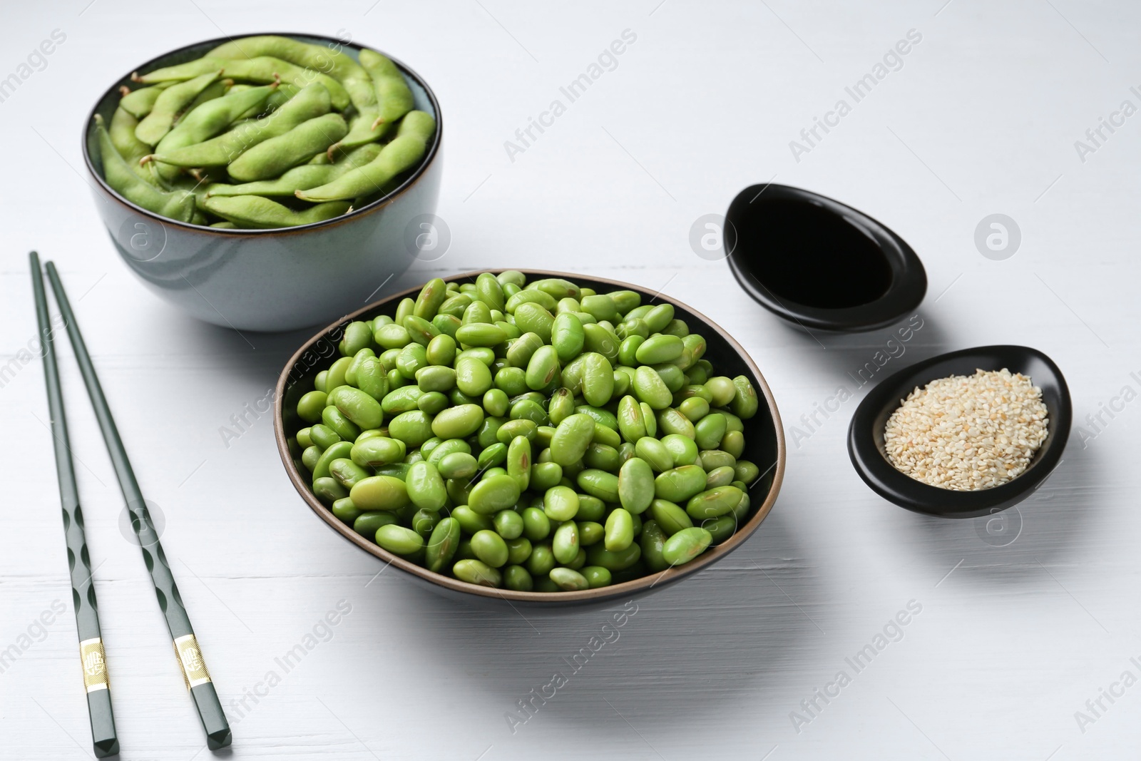 Photo of Fresh edamame soybeans, pods, soy sauce and seeds on white wooden table, closeup