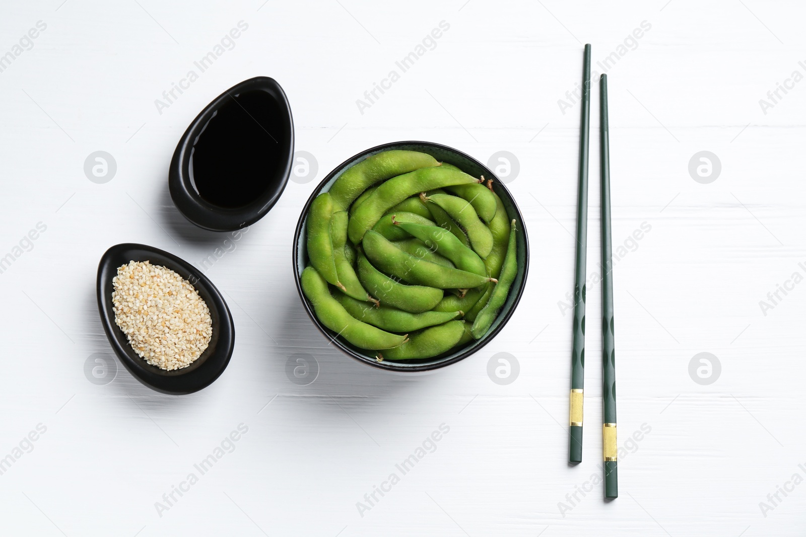 Photo of Fresh edamame pods, soy sauce and seeds on white wooden table, flat lay