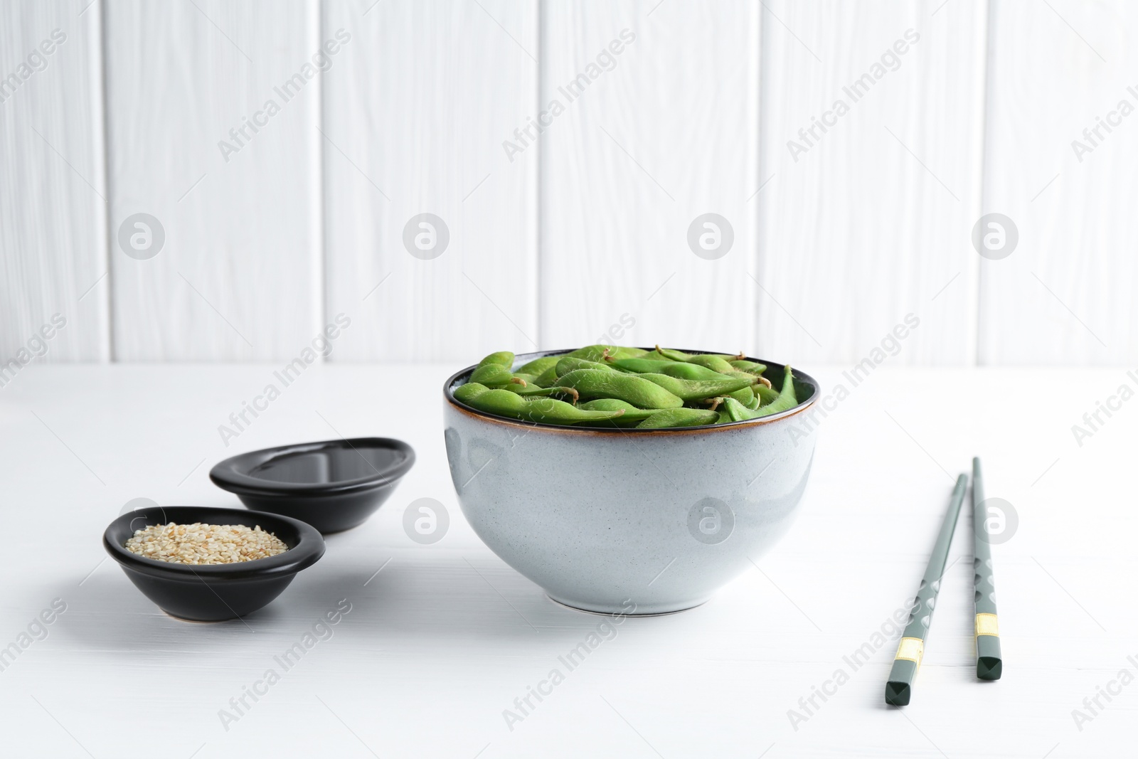 Photo of Fresh edamame soybeans, soy sauce and seeds on white wooden table