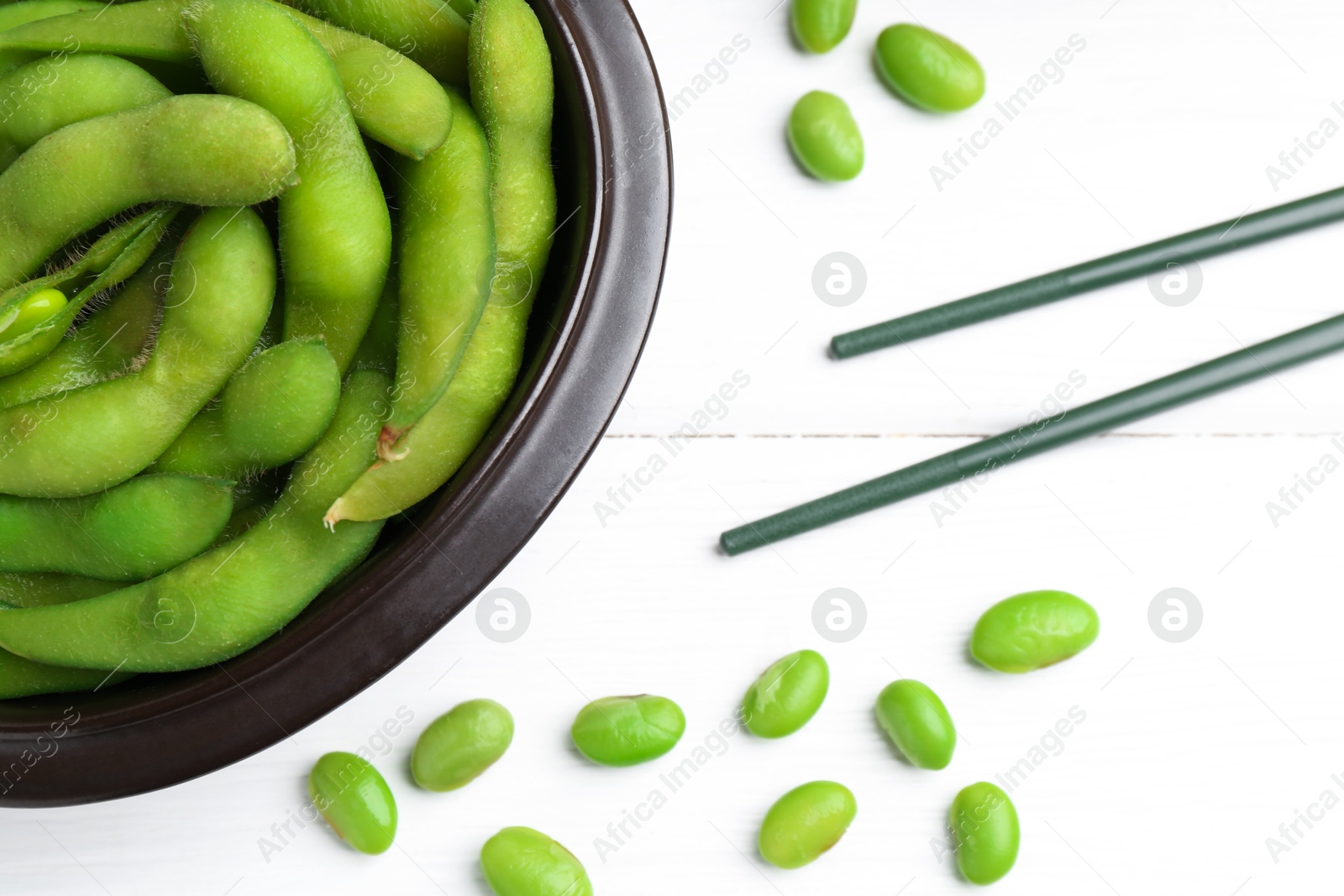 Photo of Fresh edamame pods, soybeans and chopsticks on white wooden table, flat lay