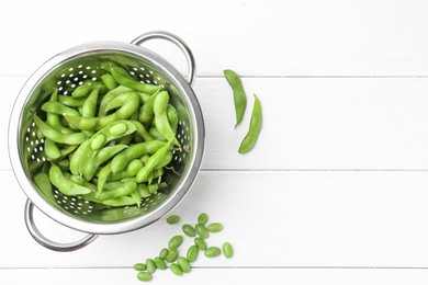 Fresh edamame pods and soybeans in colander on white wooden table, flat lay. Space for text