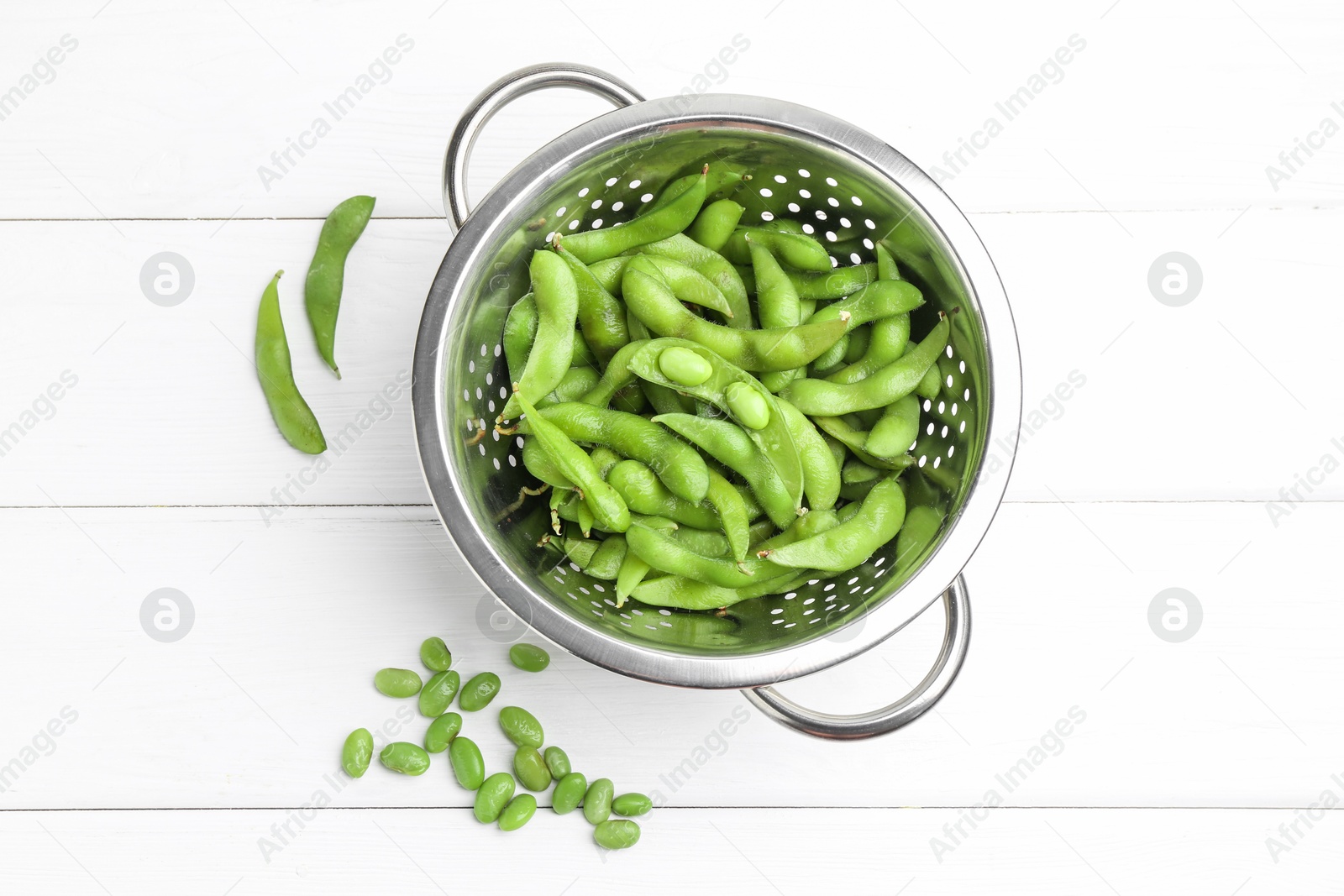 Photo of Fresh edamame pods and soybeans in colander on white wooden table, flat lay