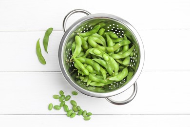 Photo of Fresh edamame pods and soybeans in colander on white wooden table, flat lay