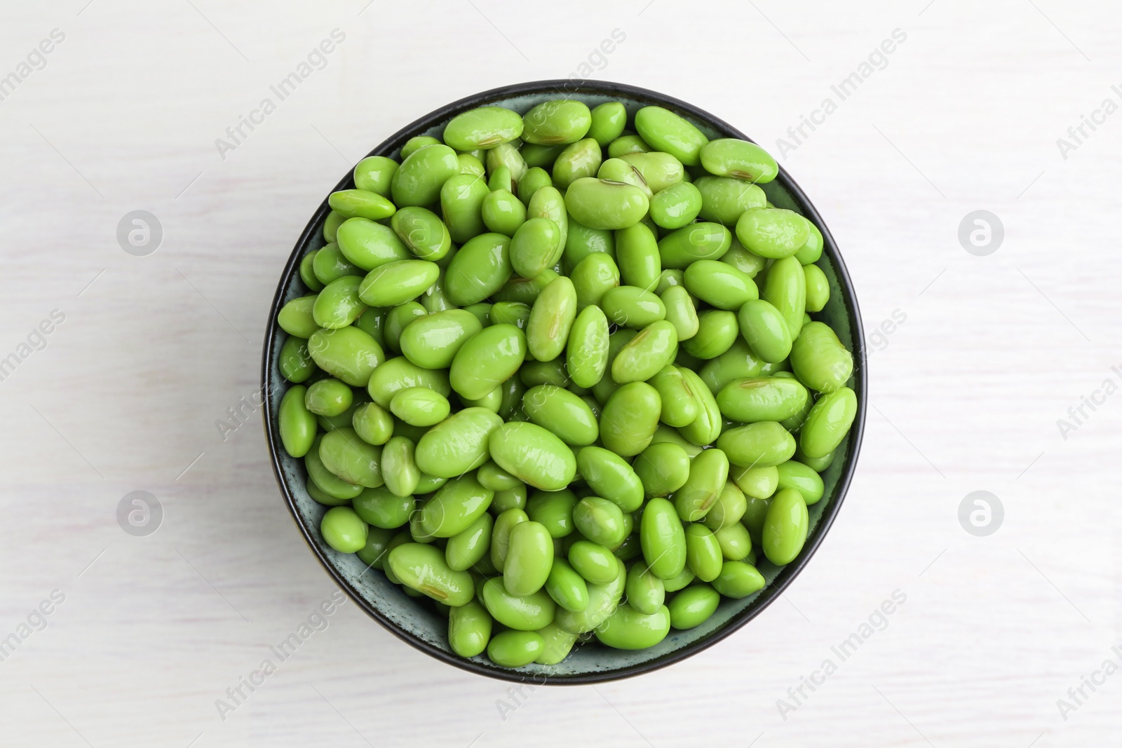 Photo of Fresh edamame soybeans in bowl on white wooden table, top view