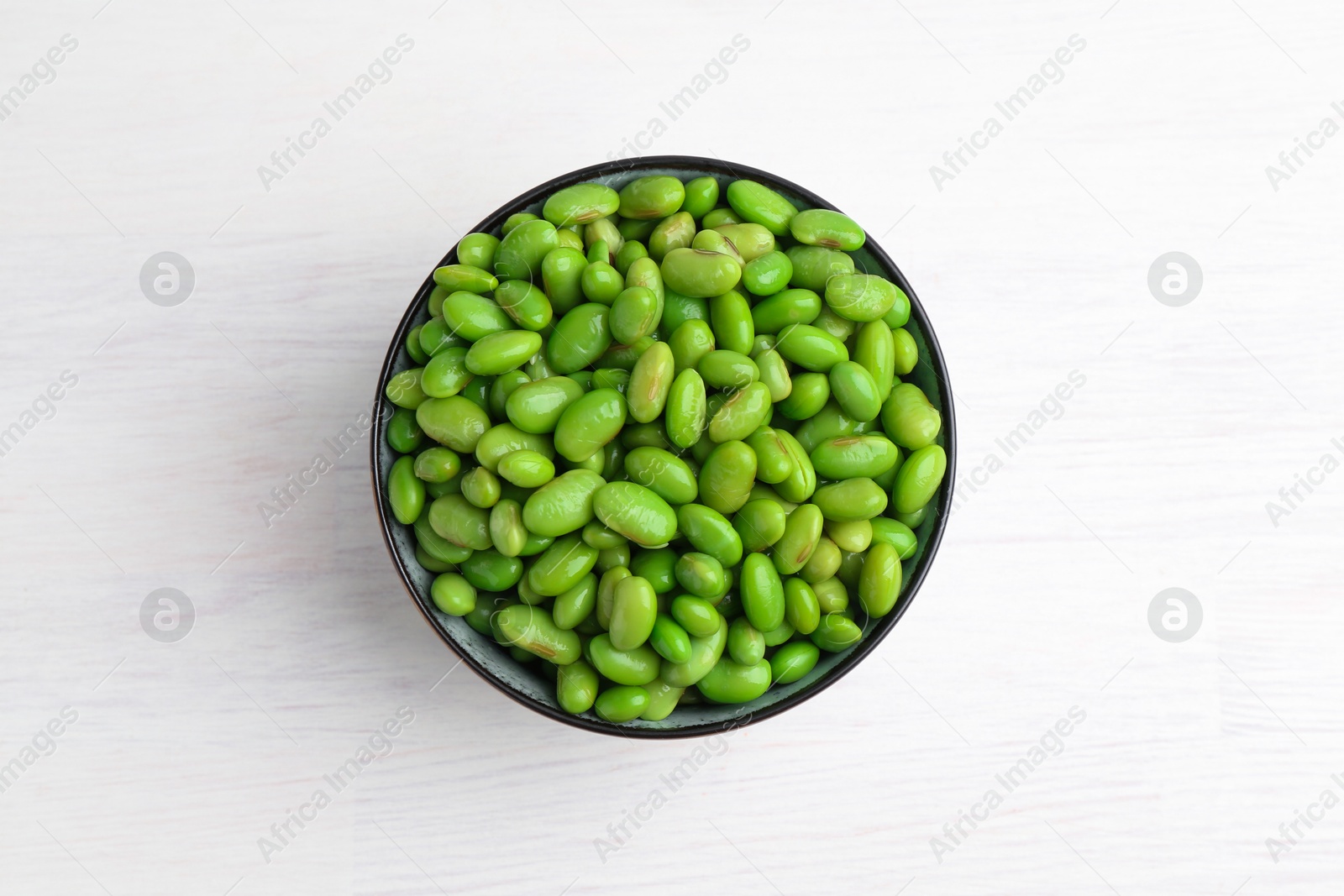 Photo of Fresh edamame soybeans in bowl on white wooden table, top view