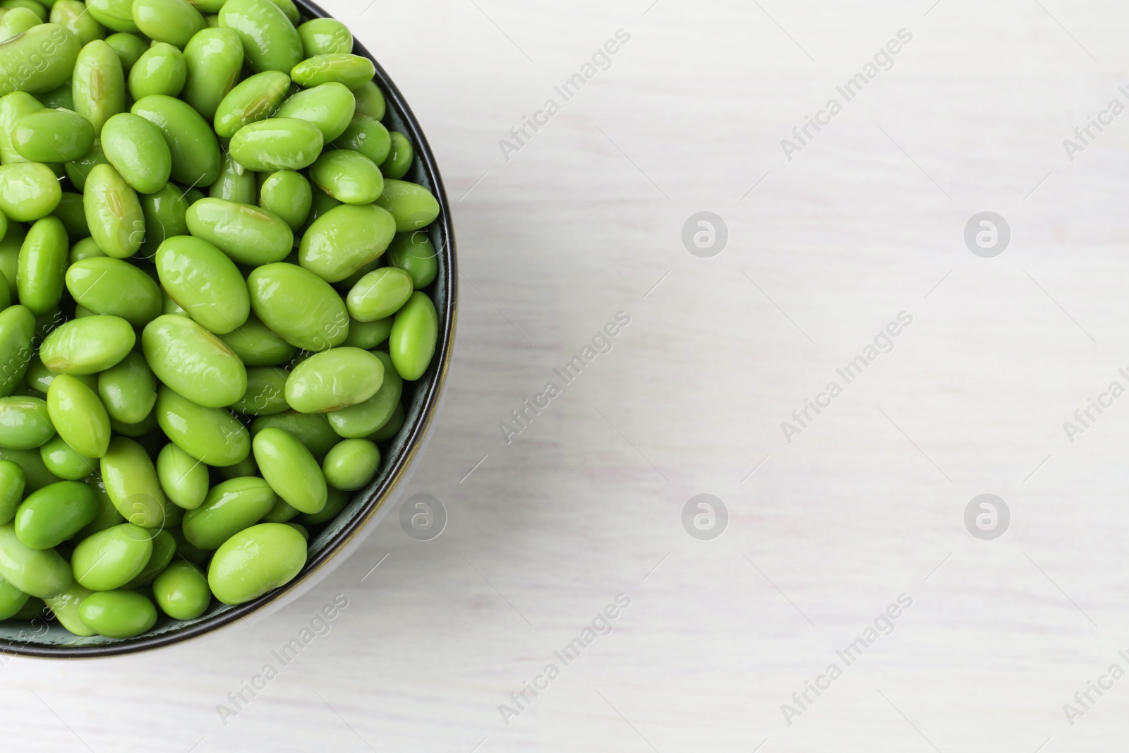 Photo of Fresh edamame soybeans in bowl on white wooden table, top view. Space for text