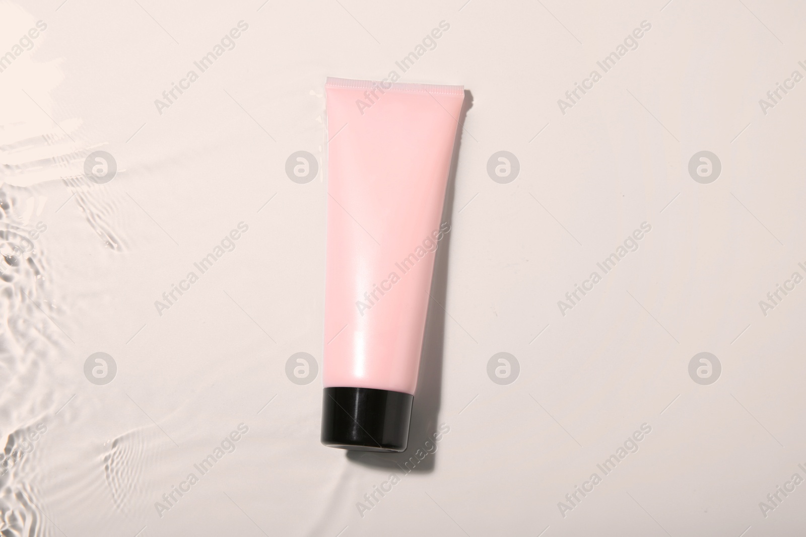 Photo of Cosmetic product. Tube with cream in water on light background, top view