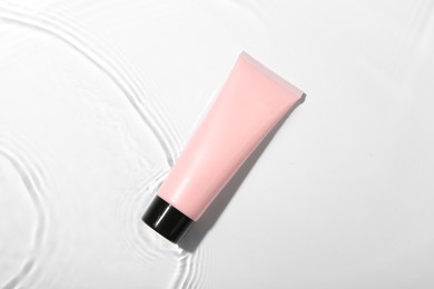 Photo of Cosmetic product. Tube with cream in water on light background, top view