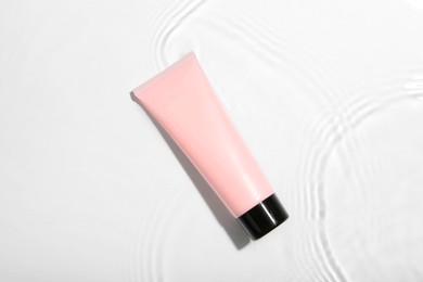 Cosmetic product. Tube with cream in water on light background, top view