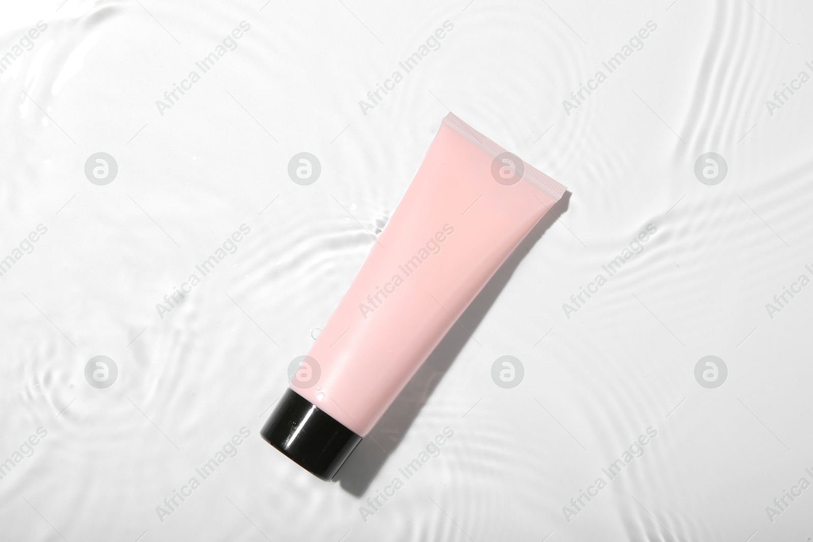 Photo of Cosmetic product. Tube with cream in water on light background, top view