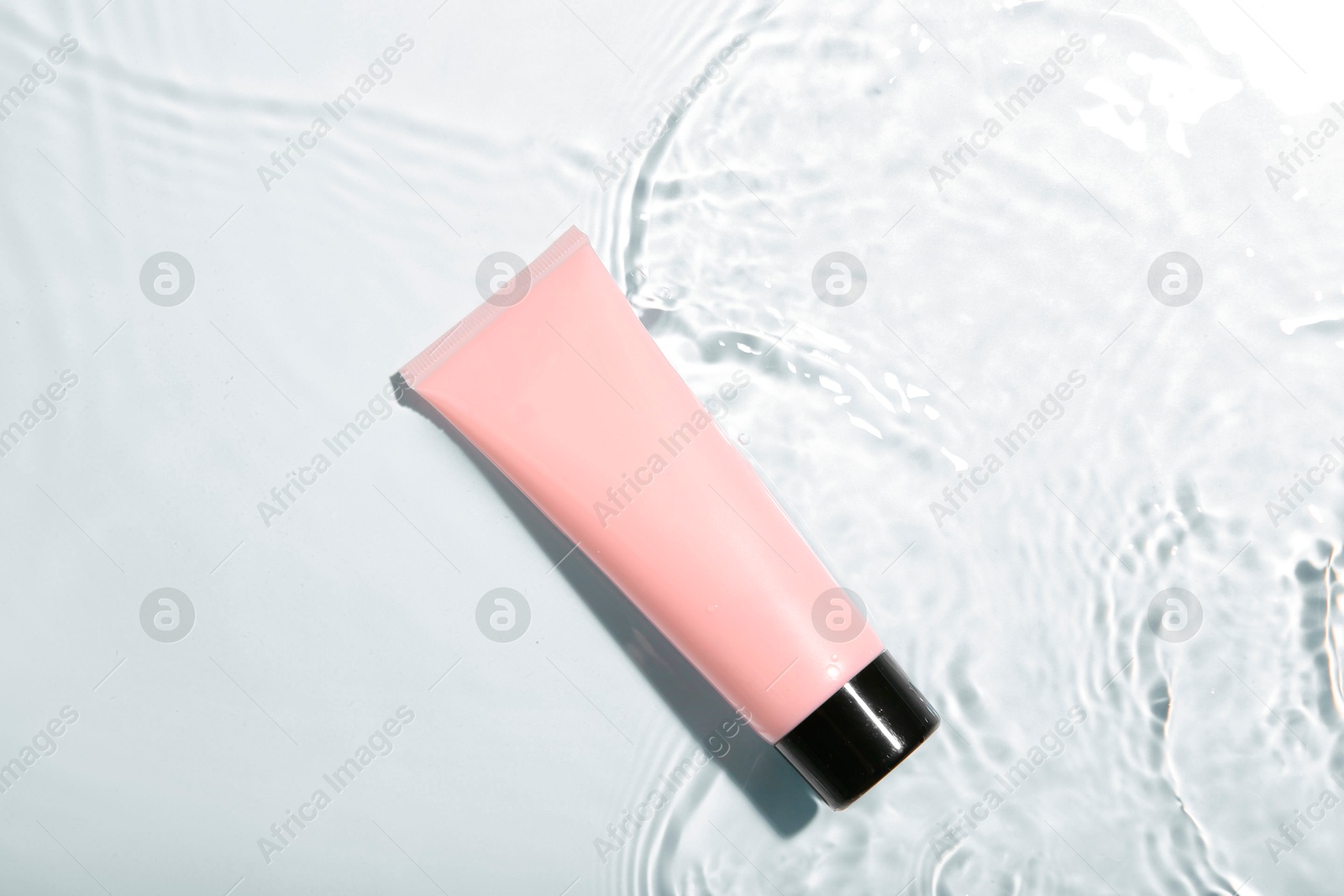 Photo of Cosmetic product. Tube with cream in water on light background, top view