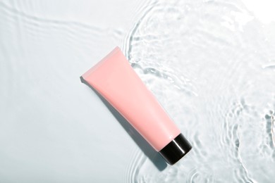 Cosmetic product. Tube with cream in water on light background, top view