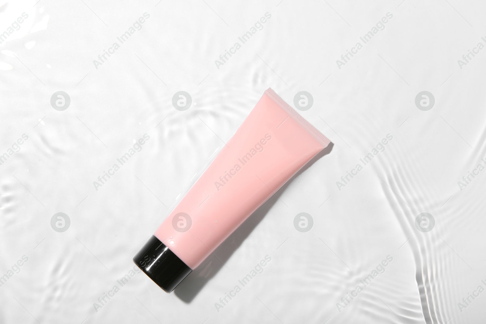 Photo of Cosmetic product. Tube with cream in water on light background, top view