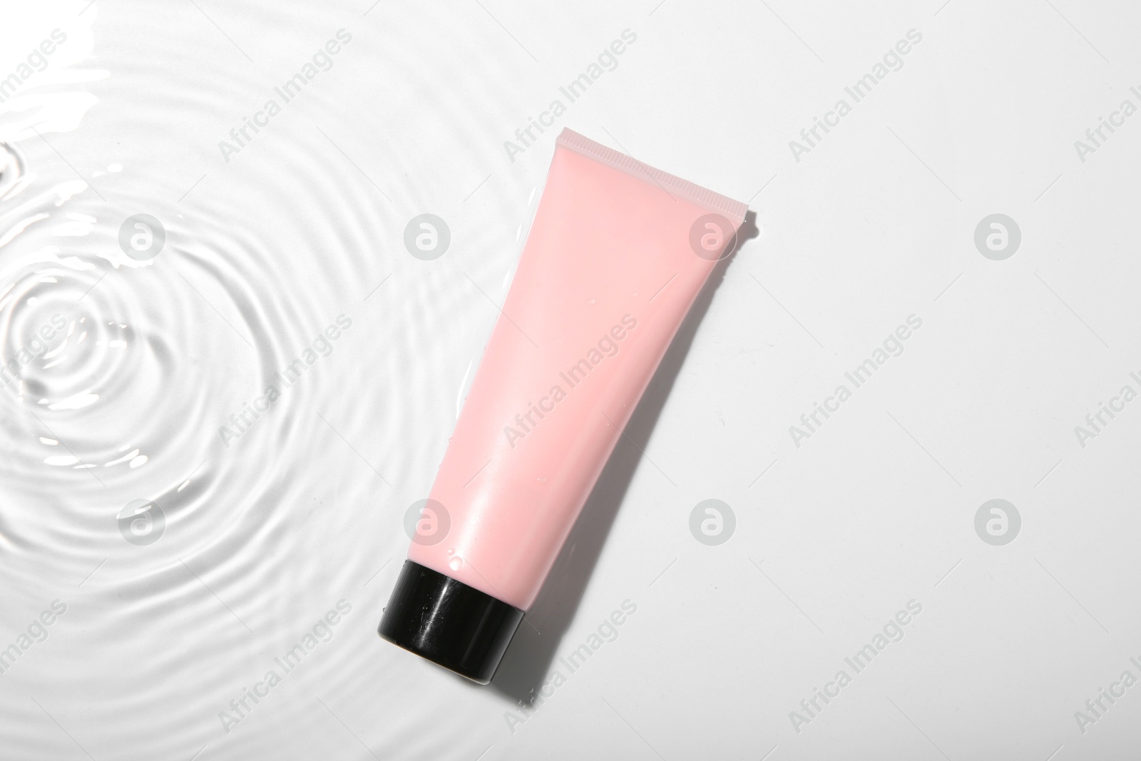 Photo of Cosmetic product. Tube with cream in water on light background, top view