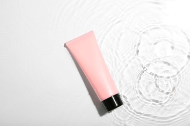 Photo of Cosmetic product. Tube with cream in water on light background, top view