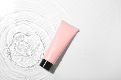 Photo of Cosmetic product. Tube with cream in water on light background, top view