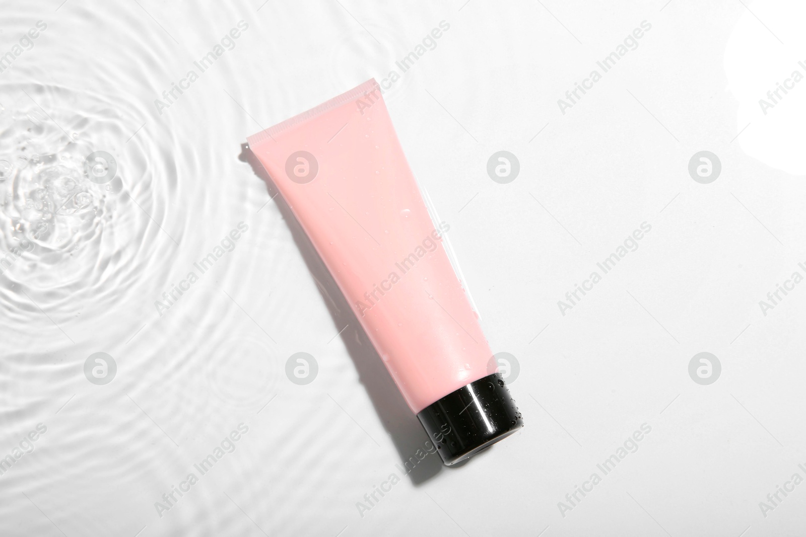 Photo of Cosmetic product. Tube with cream in water on light background, top view