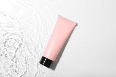 Cosmetic product. Tube with cream in water on light background, top view