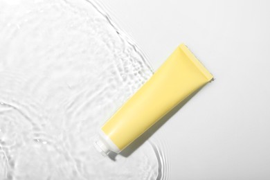 Cosmetic product. Tube with cream in water on light background, top view